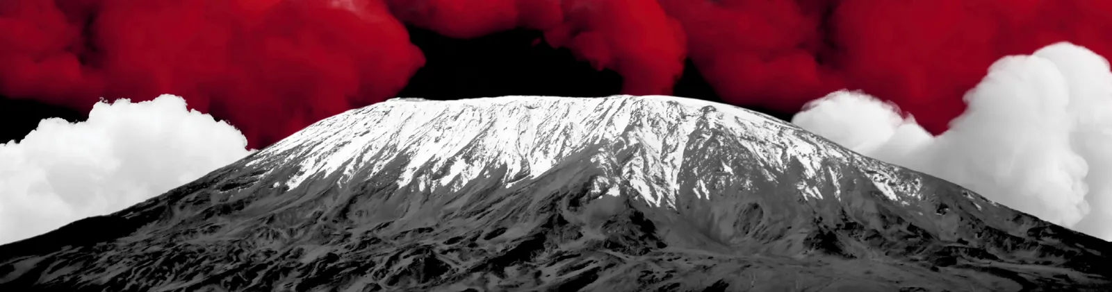Kilimanjaro’s snow-capped summit in black and white, between white clouds, under a sky of red clouds.