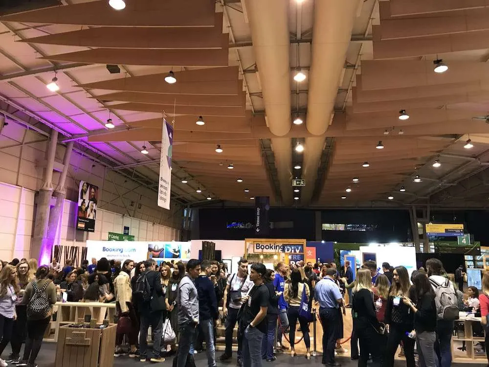 Crowds of attendees among the exhibition stands in a Web Summit hall, with Booking.com stands in the background.
