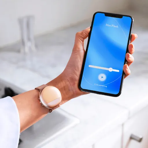 A hand holding the Embr Wave app on a phone, the Wave wristband on the wrist.