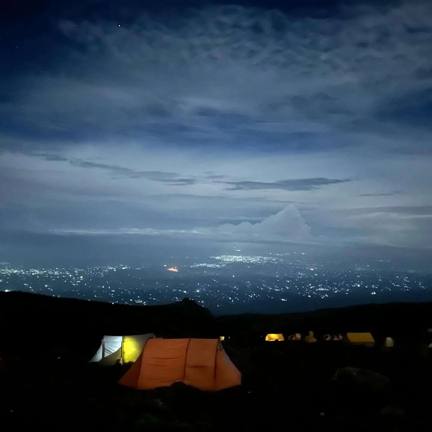 Tents glowing at camp at night, high above the lights of the towns on the plain below.
