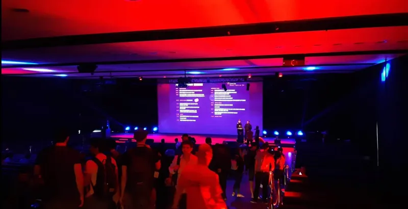 The React Native EU stage in Wroclaw under red and blue lights, the day’s schedule on the big screen as attendees take their seats.
