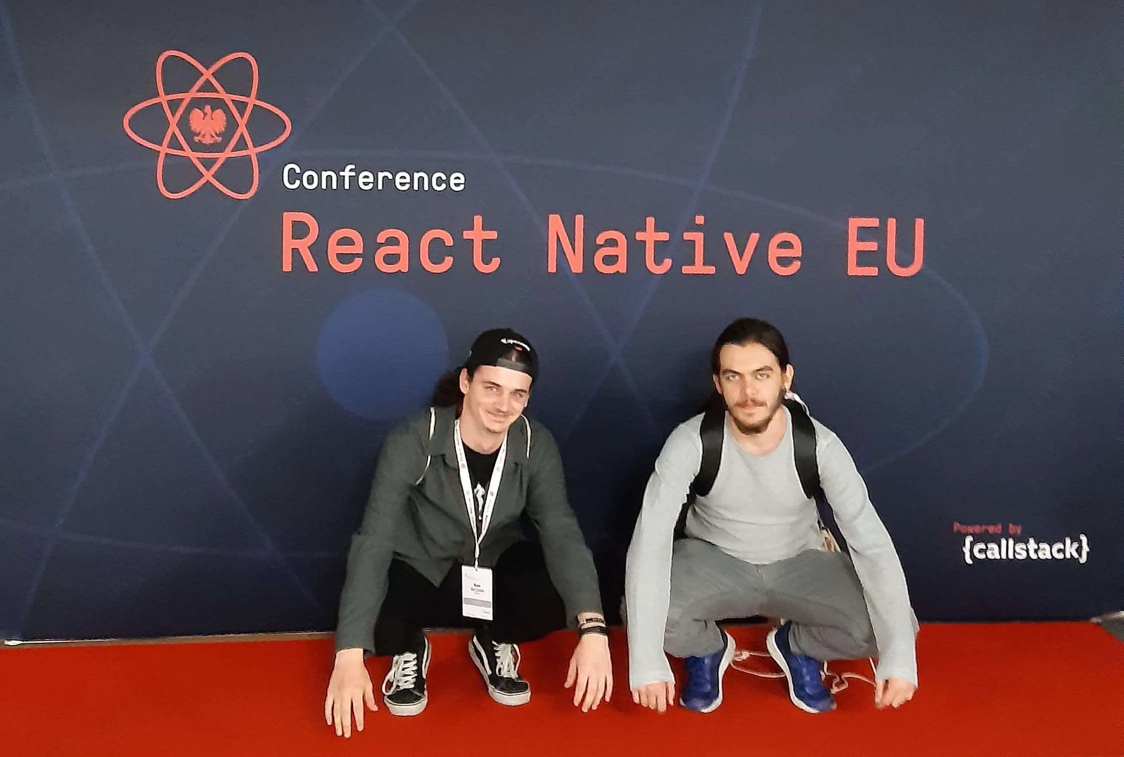 Two Salt &amp; Pepper developers crouching on a red carpet in front of the “Conference React Native EU” backdrop, powered by Callstack.