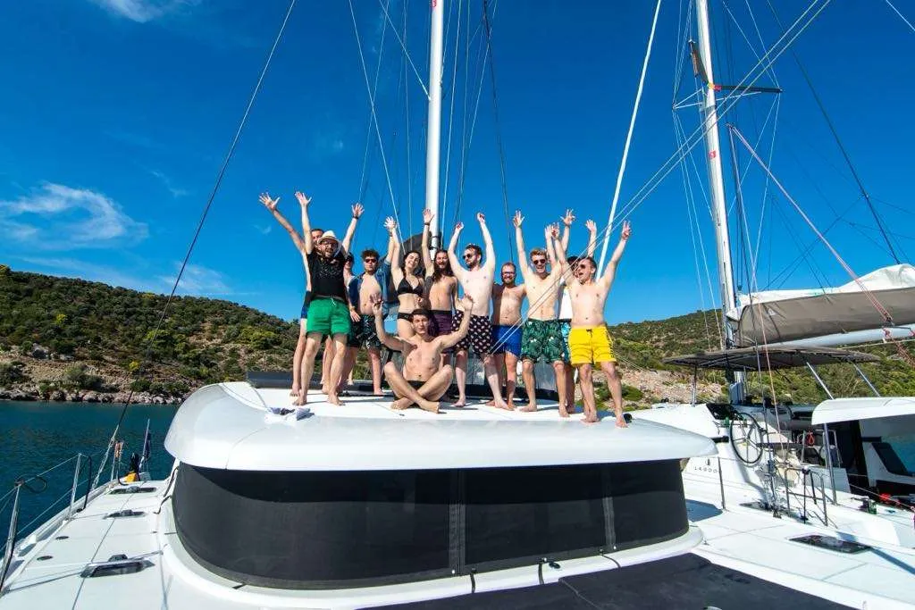 Part of the Salt & Pepper team with their arms raised on the deck of a catamaran, under a blue sky beside green hills.