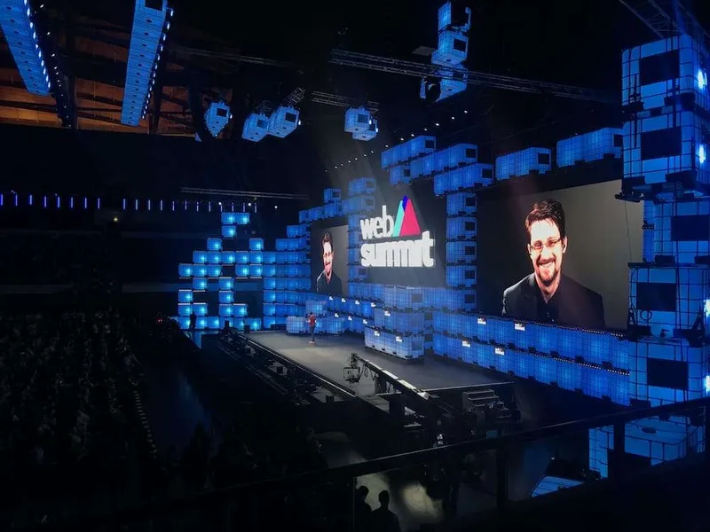 Edward Snowden on the big screens of the Web Summit centre stage in Lisbon, lit in blue beside the Web Summit logo.